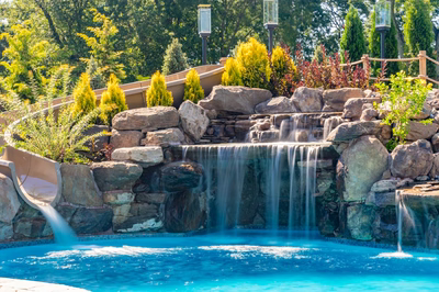 Russell C - Maple Shade, NJ - A swimming pool with a waterfall and a slide surrounded by lush greenery