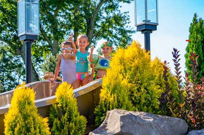 Russell J - Maple Shade, NJ - A group of children playing in a wooden toy boat in a garden setting surrounded by lush greenery and water features