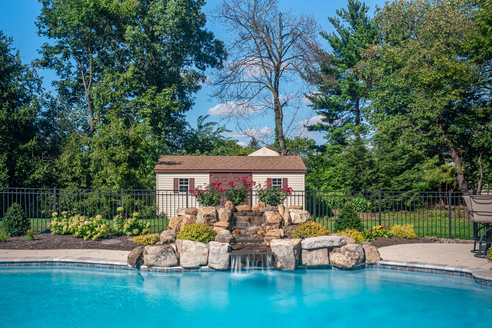 Natural stone boulder waterfall cascading into a pool surrounded by lush green plants