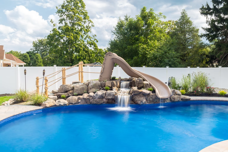 Natural stone boulder waterfall cascading into a pool with a slide and landscaping