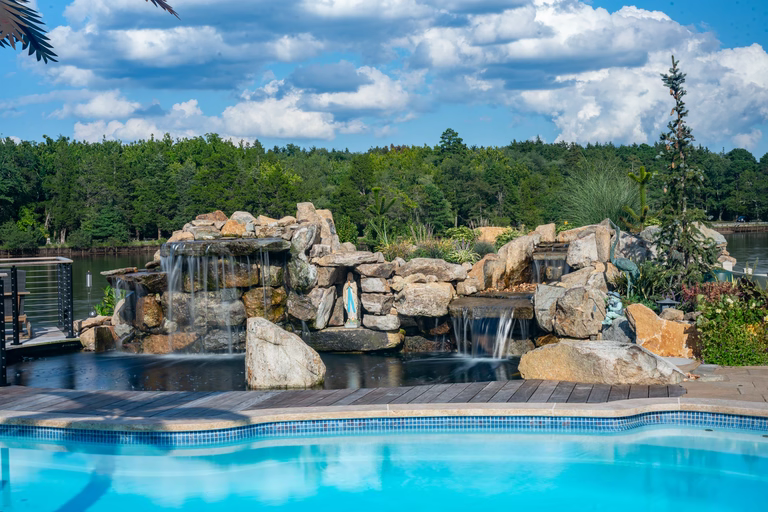 Natural stone boulder waterfalls feature cascading into a pool with lush landscaping