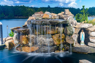 Shebelle - Hammonton, NJ - A statue of a person standing in front of a waterfall on a rocky shore of a lake