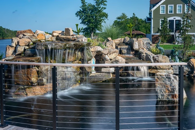 Shebelle - Hammonton, NJ - A wooden deck with a waterfall in the middle of a pond surrounded by rocks and greenery