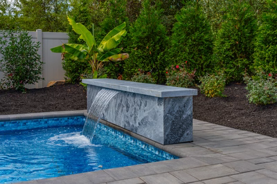Formal G -  - A rectangular pool with a waterfall feature surrounded by lush greenery and flowers