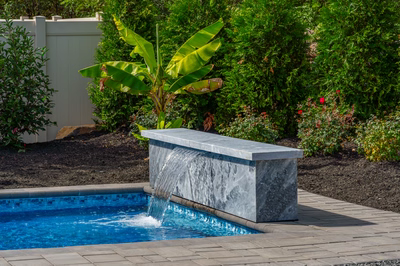 Formal G -  - A concrete bench with a waterfall in the middle of a swimming pool surrounded by lush greenery