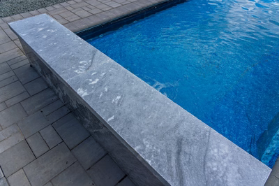 Formal G -  - A blue swimming pool with a concrete edge and pavers around it
