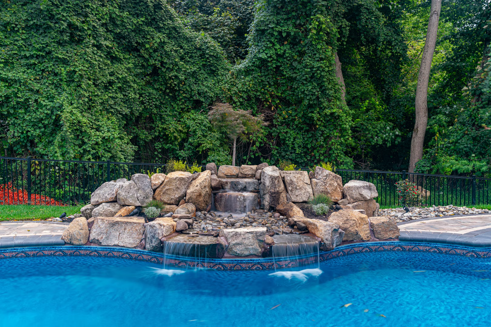 Natural stone boulder waterfall cascading into a pool surrounded by dense green foliage