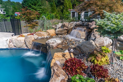 Sipi E - Pikesville, MD - A backyard with a pool and a waterfall surrounded by rocks and plants