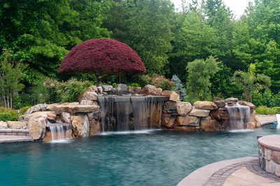 Sisiyi N - Manalapan, NJ - A large rock waterfall in the middle of a swimming pool surrounded by lush greenery