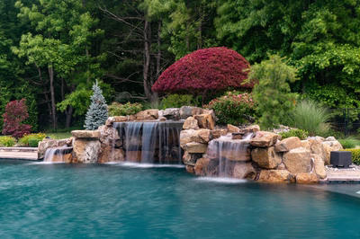 Sisiyi N - Manalapan, NJ - A beautiful landscape with a waterfall in the middle of a swimming pool surrounded by lush greenery