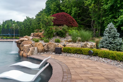 Sisiyi N - Manalapan, NJ - A scenic landscape with a rock garden and a swimming pool surrounded by lush greenery