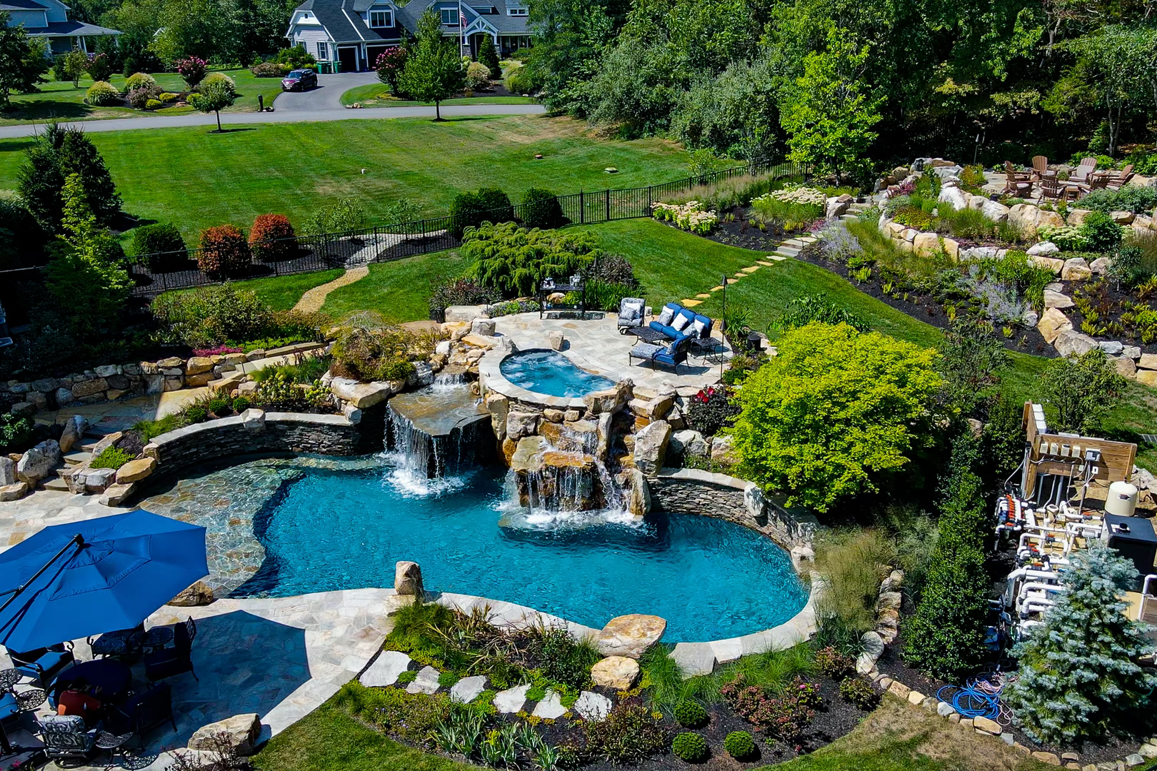 Multi-tiered stone boulder waterfall cascading into a freeform pool surrounded by lush garden plants