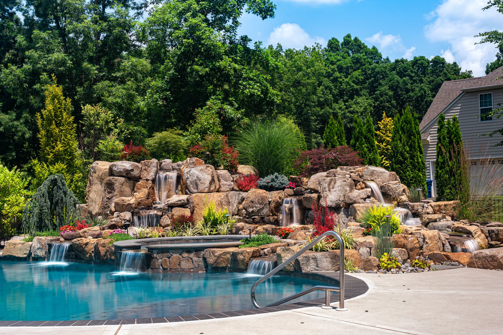 Natural stone boulder waterfalls cascade into a pool surrounded by lush, colorful landscaping