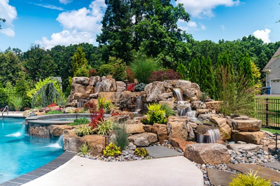Spray E - Franklinville, NJ - A backyard with a pool and a waterfall feature surrounded by lush greenery
