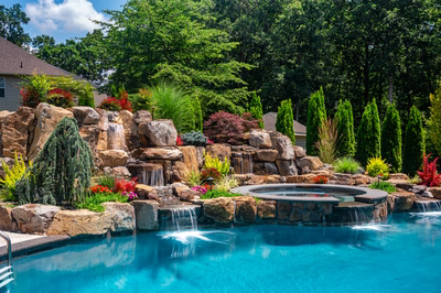 Spray J - Franklinville, NJ - A swimming pool with a waterfall feature surrounded by lush greenery and colorful flowers