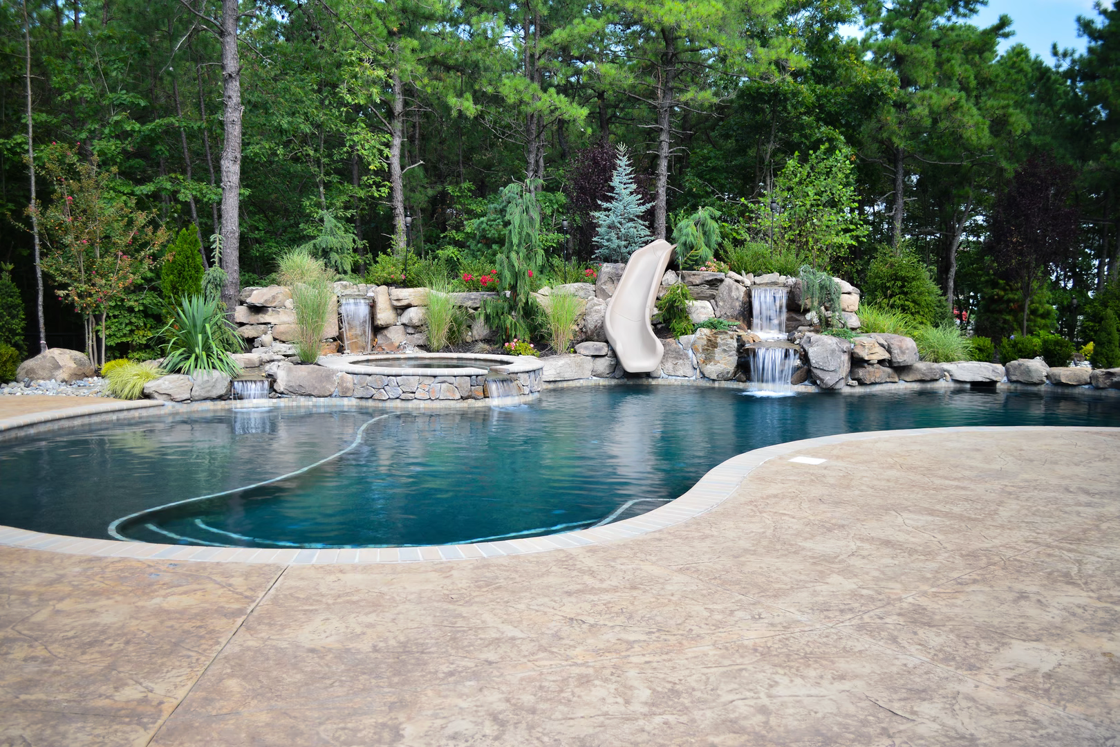 Natural stone boulder waterfalls cascading into a freeform pool surrounded by lush greenery