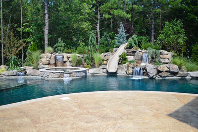 Sutherland B - Monroe, NJ - A swimming pool with a waterfall and a slide surrounded by lush greenery