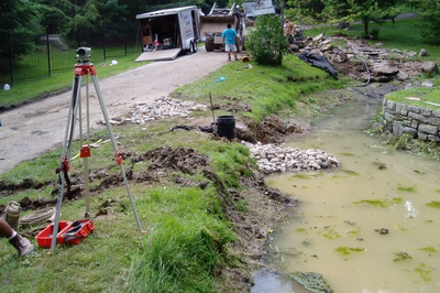 Swiftwater F - Pennsylvania - A surveying device on a tripod next to a muddy stream in a grassy area.