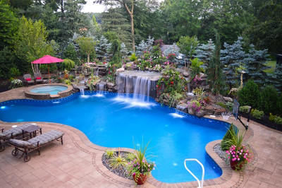 Tama A - Manalapan, NJ - A swimming pool with a waterfall surrounded by lush greenery and colorful flowers