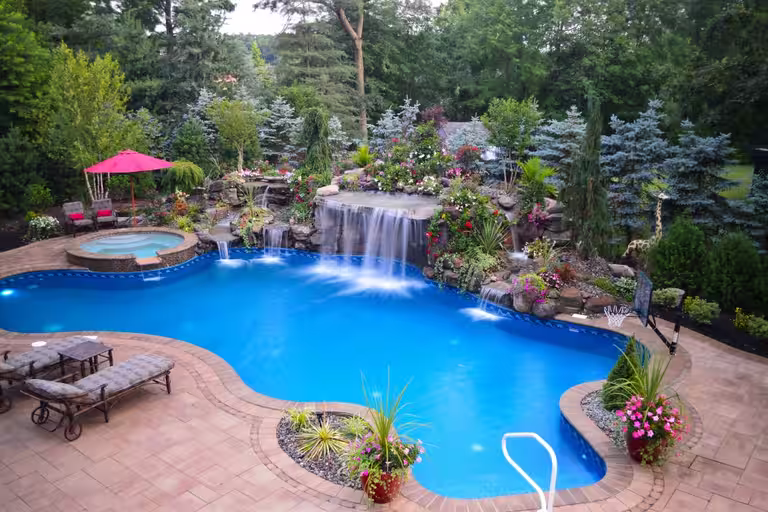 Natural stone boulder waterfalls cascading into a freeform pool with lush floral landscaping