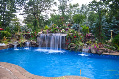 Tama C - Manalapan, NJ - A swimming pool with a waterfall surrounded by lush greenery and colorful flowers
