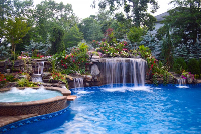 Tama D - Manalapan, NJ - A swimming pool with a waterfall surrounded by lush greenery and colorful flowers