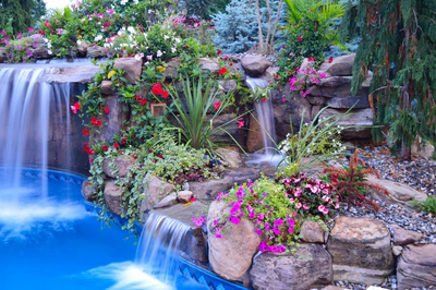 Tama G - Manalapan, NJ - A swimming pool with a waterfall surrounded by lush greenery and colorful flowers