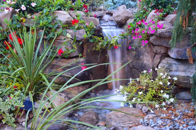 Tama I - Manalapan, NJ - A swimming pool with a waterfall surrounded by lush greenery and colorful flowers