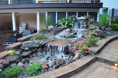 Tama N - Manalapan, NJ - A small waterfall surrounded by flowers and rocks in a backyard setting