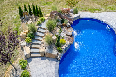 Tamolitch H - Millstone, NJ - A swimming pool with a waterfall and a slide surrounded by landscaping