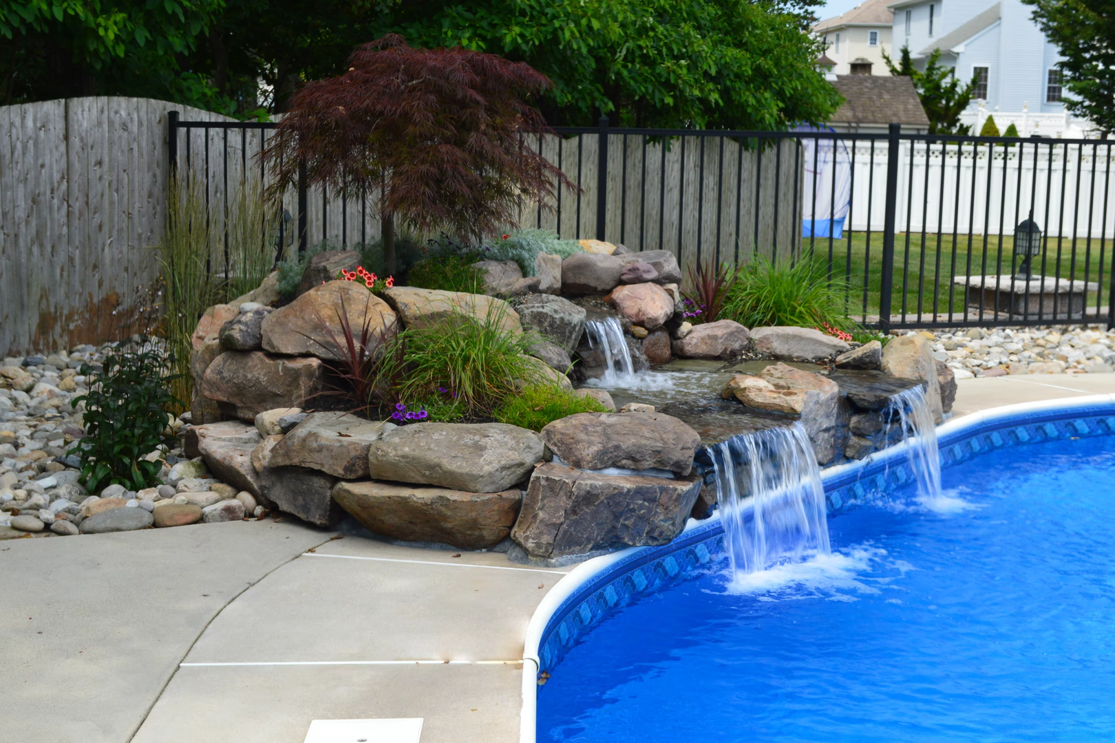 Natural stone boulder waterfall cascading into a pool surrounded by lush garden greenery
