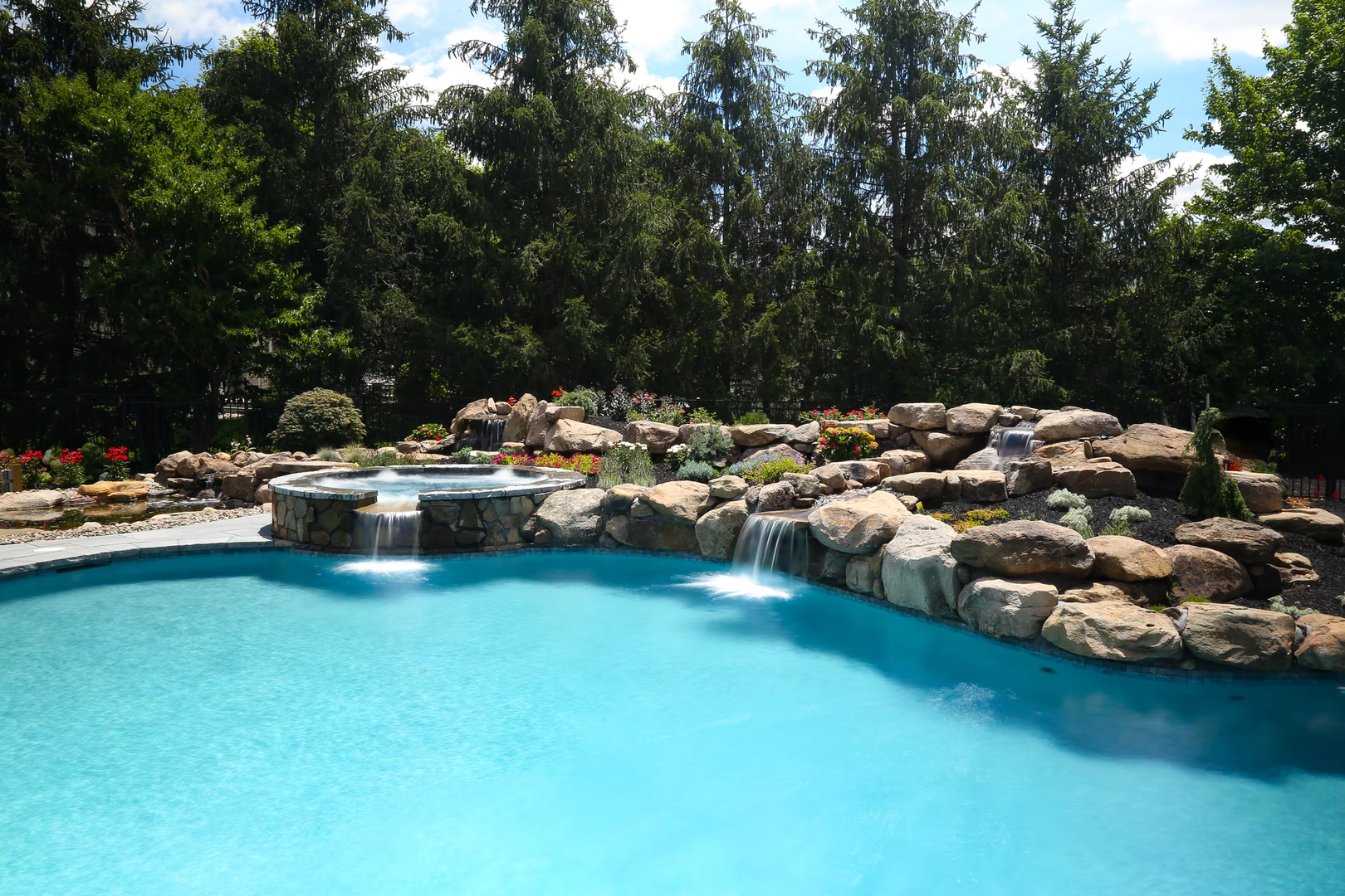 Natural stone boulder waterfalls cascade into a pool surrounded by lush green trees