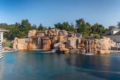 Tchupala B - Medford, NJ - A large rock pool with a waterfall and a slide in a backyard setting