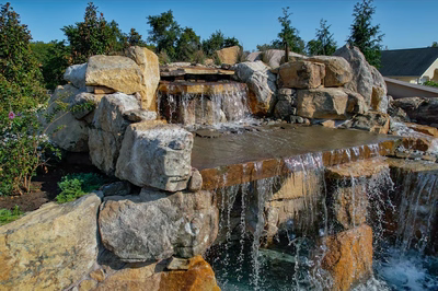 Tchupala H - Medford, NJ - A large rock waterfall in a backyard setting with a house in the background