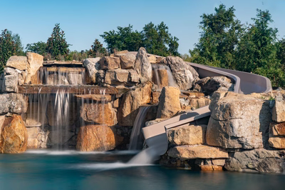 Tchupala J - Medford, NJ - A large rock waterfall with a slide in the middle of a pool surrounded by lush greenery