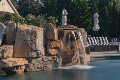 Tchupala L - Medford, NJ - A large rock waterfall in the middle of a swimming pool surrounded by lounge chairs and umbrellas