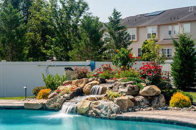 Thika B - Berlin, NJ - A backyard with a waterfall and landscaping around a swimming pool