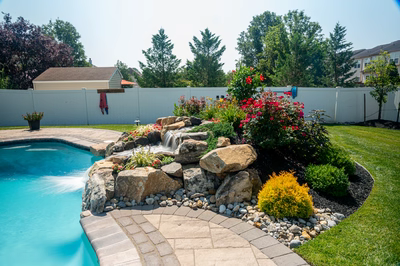 Thika C - Berlin, NJ - A backyard with a pool and a waterfall surrounded by flowers and landscaping
