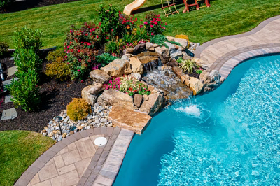 Thika F - Berlin, NJ - A backyard with a swimming pool and a waterfall surrounded by flowers and landscaping