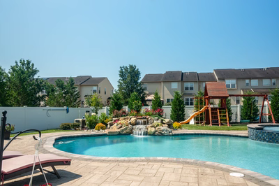 Thika J - Berlin, NJ - A backyard with a swimming pool, a play structure, and a waterfall