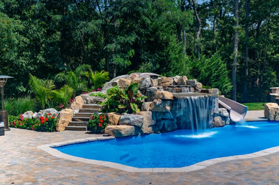 Toketee C - Galloway, NJ - A swimming pool with a waterfall and a water feature surrounded by lush greenery