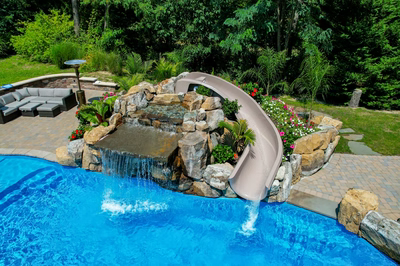 Toketee D - Galloway, NJ - A swimming pool with a water feature and a slide surrounded by lush greenery