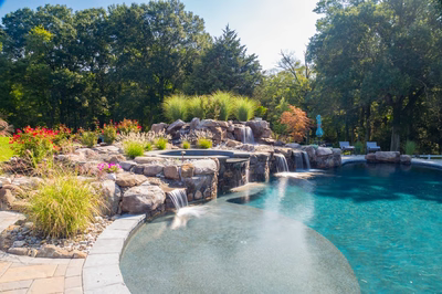 Tufa C - Medford, NJ - A swimming pool with a waterfall in the middle surrounded by lush greenery and colorful flowers