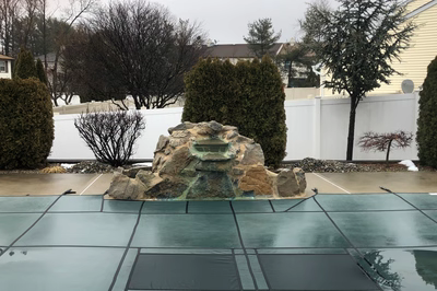 Tugela A - Sayreville, NJ - A large rock fountain in the middle of a snow-covered backyard with a white fence surrounding it
