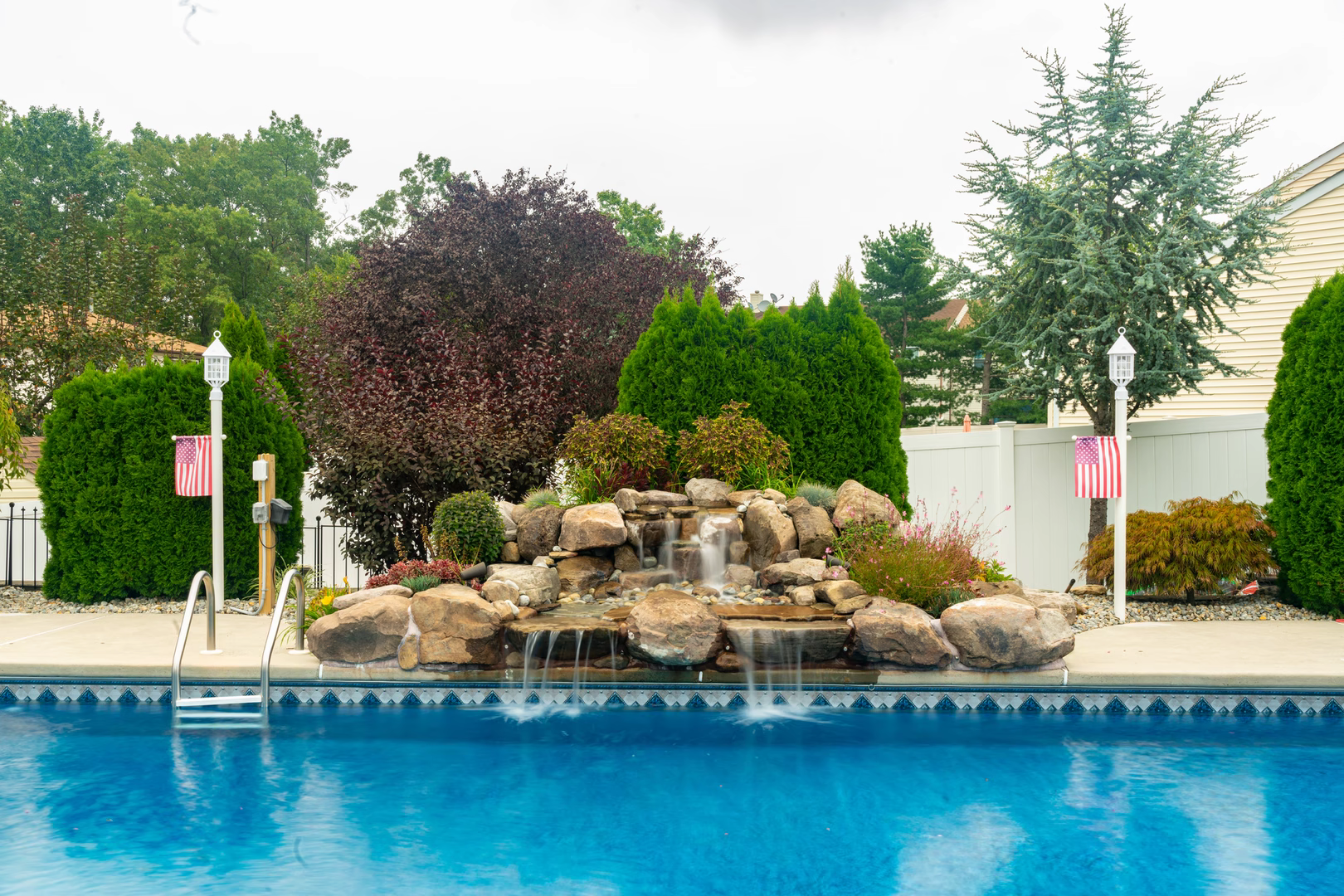 Natural stone boulder waterfall cascading into a pool surrounded by lush green plants