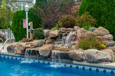 Tugela G - Sayreville, NJ - A swimming pool with a waterfall feature surrounded by lush greenery and flowers