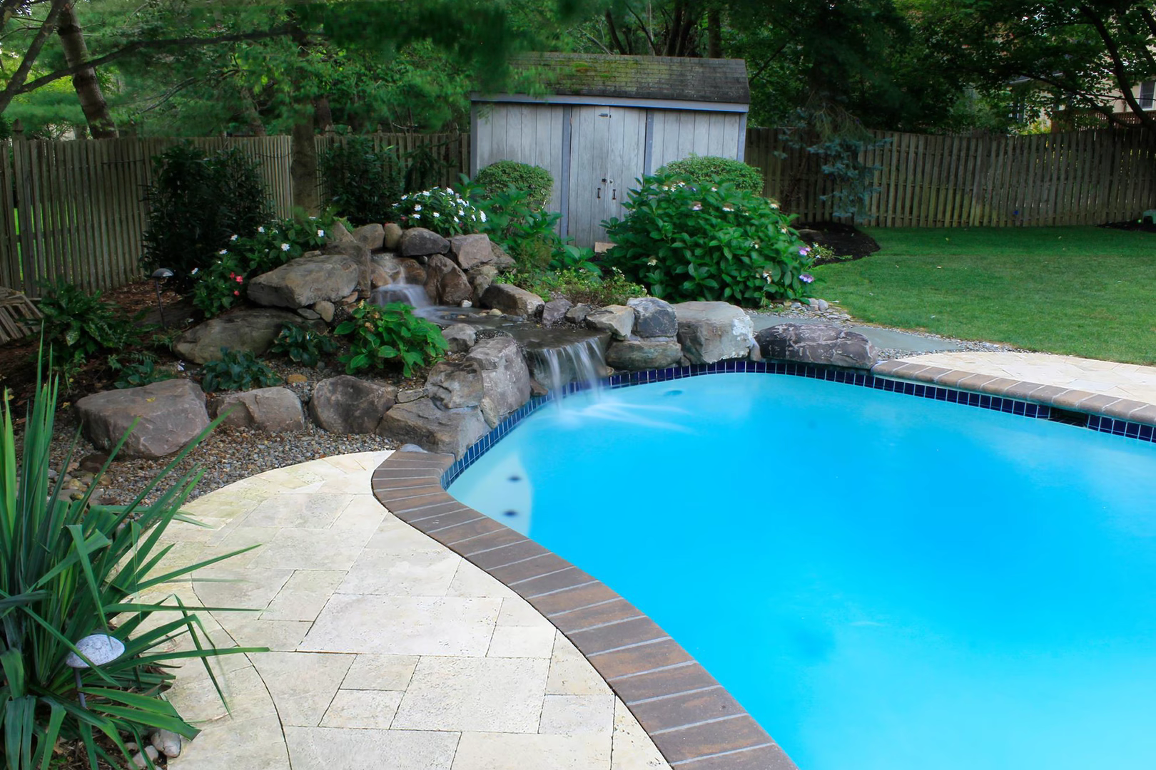 Natural stone boulder waterfall cascading into a blue pool surrounded by lush greenery