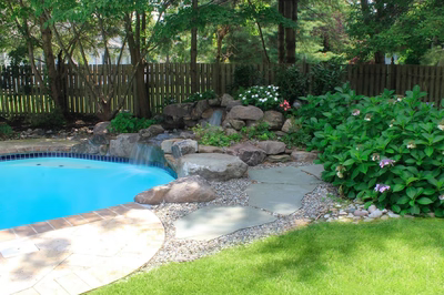 Tully D - Voorhees, NJ - A backyard with a pool and a waterfall surrounded by greenery and flowers