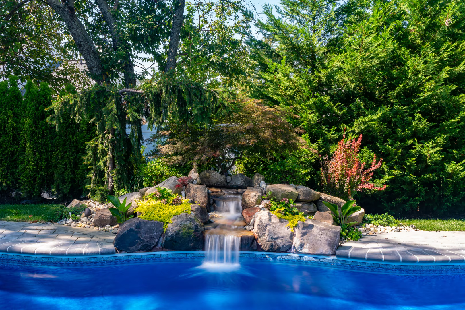 Natural stone boulder waterfall cascades into a blue pool surrounded by lush greenery