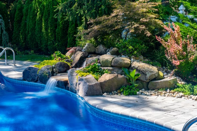 Tumalo B - Freehold, NJ - A swimming pool surrounded by lush greenery and rocks with a waterfall